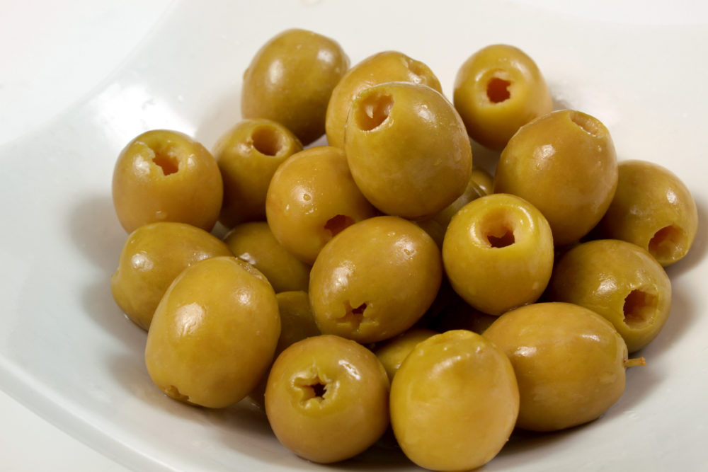 A close-up shot of a white dish filled with pitted naturally-cured green olives