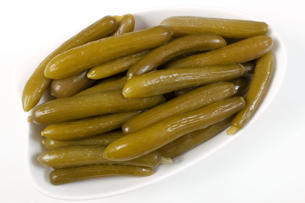 Around two dozen short, slender pickled cucumbers on a white dish